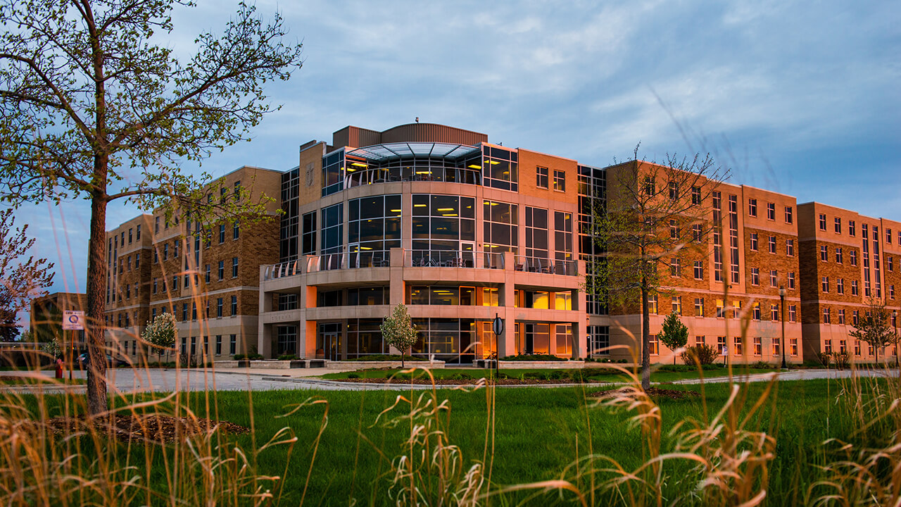 Peeking through the tall bluff grass, the morning sun provides a warm glow onto Coburg Residence Hall.