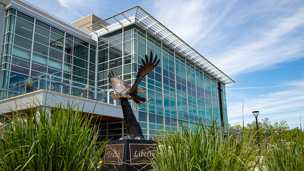 A front exterior view of the Robert W. Plaster Free Enterprise Center; in front of which is a large bald eagle statue. Inscribed on each side of its base are the words: Faith, Truth, Liberty, and Economics.