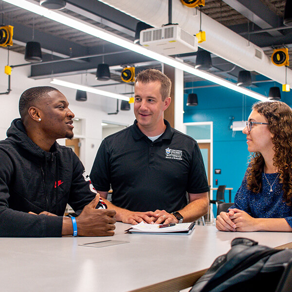 A professor talks to two students in the Collaboratorium.