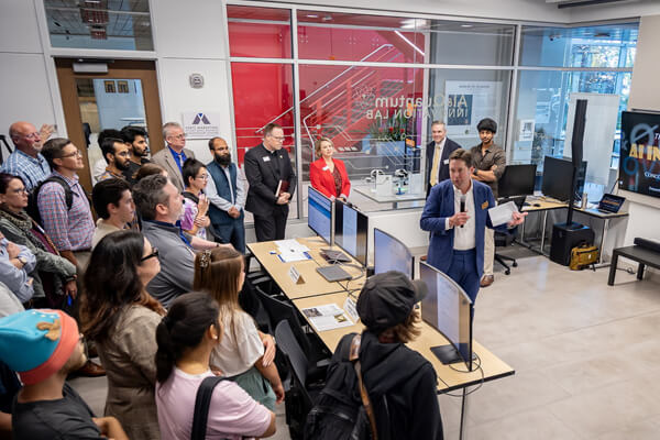 A group of attendees gathers in the CUW AI & Quantum Innovation Lab as a presenter speaks during the November 5, 2025 pitch event. Several computer stations and lab equipment are visible in the room.
